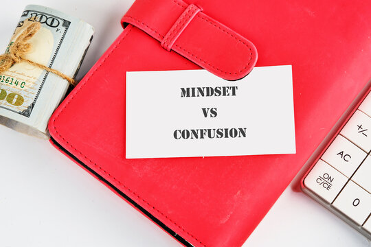 A bright red notebook rests on a table beside a stack of cash and a calculator, highlighting the clash between focused thinking and the chaos of confusion in financial choices