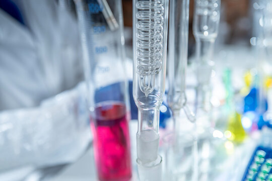 Close up of a gloved hand holding a glass rectification fractionating column among laboratory glassware. Concept for distillation, chemical engineering and analytical chemistry, copy space.