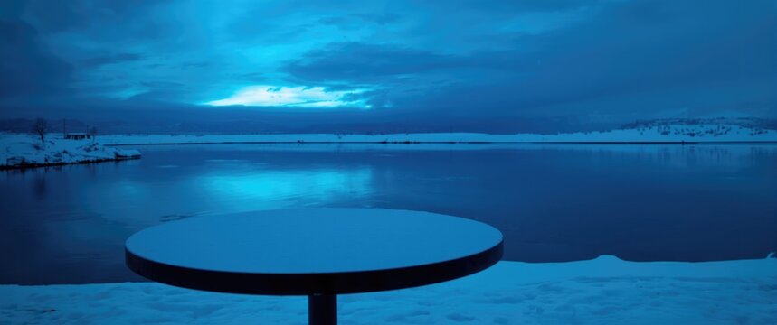 Quiet snowy scene with a table in the forefront and electric blue sky reflection on water