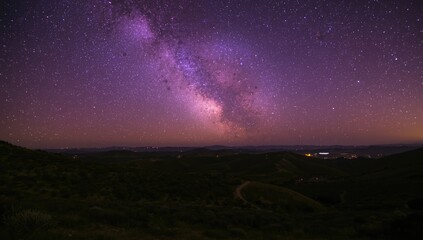 Fototapeta premium Summer hills under a brilliant purple Milky Way with scattered red city glow at night