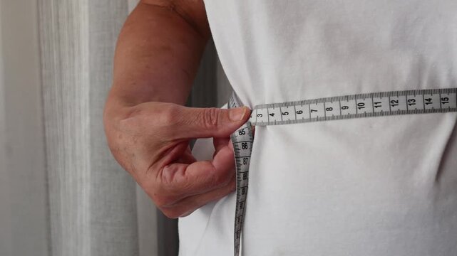 Senior woman measuring waist circumference with tape measure, weight management and healthy lifestyle concept.