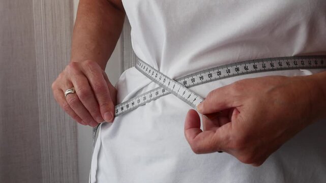 Senior woman measuring waist with tape measure, weight control and healthy lifestyle concept.