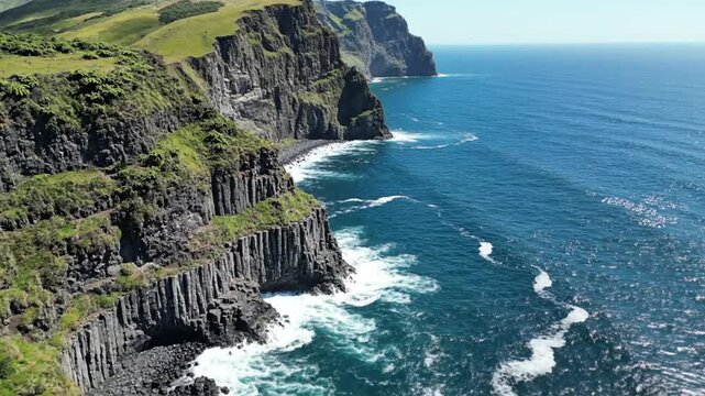 Scenic aerial view of dramatic cliffs along a vibrant blue ocean with sunlight and pristine natural beauty