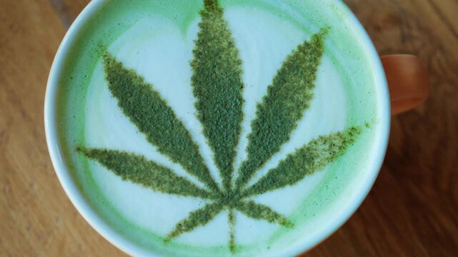 Top view of a matcha latte in a ceramic cup, decorated with powdered green tea forming a leaf pattern resembling a cannabis leaf