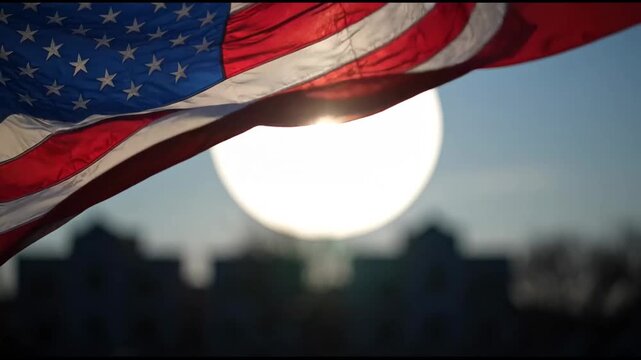Close-up of the American flag waving gracefully in front of a bright, setting sun with blue sky