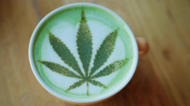 Top view of a matcha latte in a ceramic cup, decorated with powdered green tea forming a leaf pattern resembling a cannabis leaf