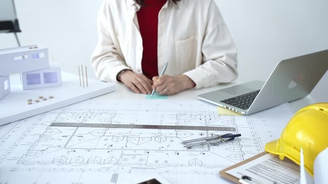 Architect working on new residential project using laptop, reviewing blueprints and drafting floor plans for modern building design with a 3d model on office desk