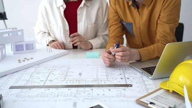 Engineering team collaborating on architectural blueprints, reviewing construction plans, and discussing building design concepts with tools and safety hard hat on table