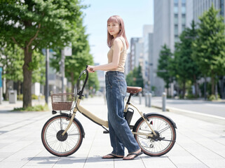 Obraz premium A young woman walking on the sidewalk in the city, pushing her bicycle. 歩道を自転車を押しながら歩く若い女性