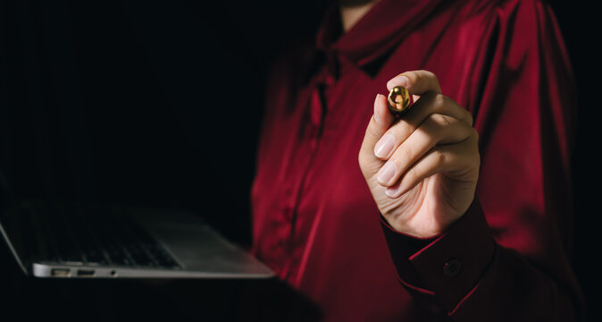 Person holding pen with laptop business concept close up of hand writing or pointing dark background professional attire red shirt technology communication office work focus hand selective focus