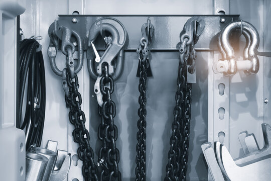wall supports metal bar. chains hang from hooks on the bar. Black chains dangle below ones. chain hook stands out prominently. Black cables coil on the wall