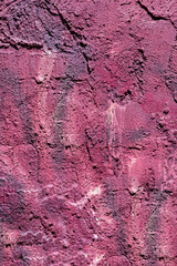 Fototapeta premium Full frame view of a weather damaged purple plaster wall showing rough uneven texture cracks and dark stains.