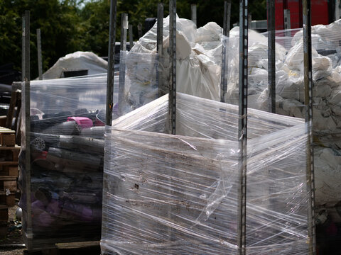 A detailed close-up shot 
of commercial nursery materials stored 
outside. Large metal cage pallets are 
filled to the top with assorted plastic 
cultivation flower pots in black, grey, 
and pink tone