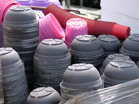 A close-up detailed shot 
highlighting large stacks of plastic flower 
pots packed together tightly. Dominating 
the foreground are upside-down grey 
pots, while vibrant pink, magenta, 
purple, and re