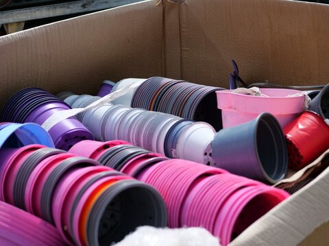 A close-up studio style 
shot looking into a large cardboard 
shipping box filled with organized stacks 
of multi-colored plastic flowerpots. The 
tightly nested containers display a rich 
palette of 