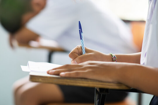 Close-up of Student Writing Exam with Classmate Sleeping in Background