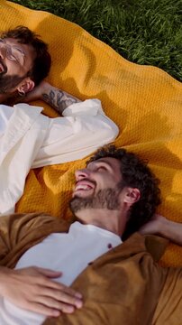Loving lgbt couple lying in city park having fun and enjoying each other presence.
Happy men gay feeling free and carefree. Male romantic couple talking with smile
about something and flirting
