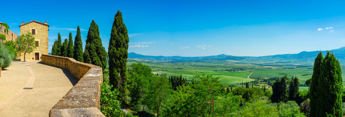 Naklejka premium Wide panoramic view of the hills and countryside surrounding the village of Pienza (Tuscany village, Italy) seen from its medieval fortified walls, during early summertime.