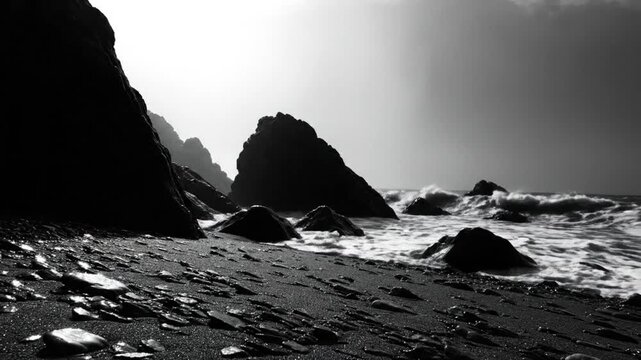 Dramatic monochrome seascape showing dark coastal rocks and powerful waves crashing on the shoreline under a bright sky