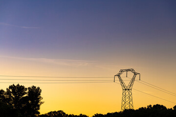 Obraz premium High voltage pylon in the French countryside stands out against the sky at sunset. 400 kV High voltage electric power grid.