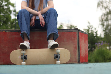 Legs of skateboarder in white sneakers and baggy jeans standing on skateboard in skate park. Concept of street style, youth culture and outdoor activities. Young girl resting with skateboard © Mariia