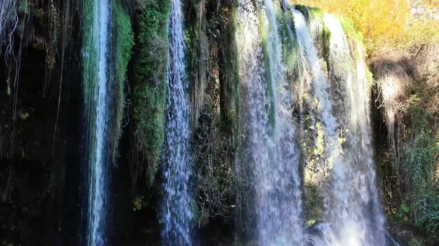 Scenic duden waterfall cascade over tall mossy rock wall with golden autumn foliage and blue sky antalya.