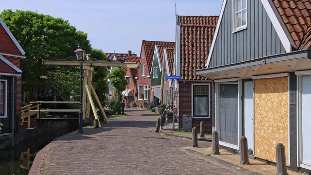 olendam, Netherlands - 31 May 2026: Quiet historic street with traditional brick paving, green wooden houses, and a classic white drawbridge over a canal on a sunny day.