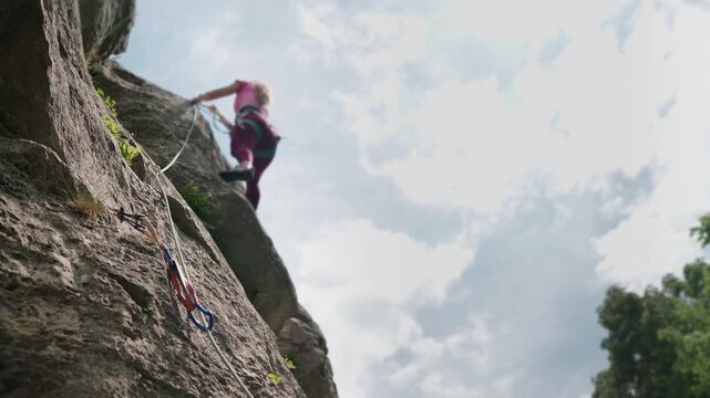 4K close up of a quickdraw on a rock wall with a moving climbing rope. Unfocused female climber ascending a steep cliff on the background of extreme sport safety gear concept