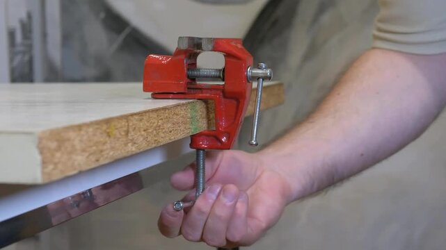 A worker clamps a vise onto a workbench in a workshop.