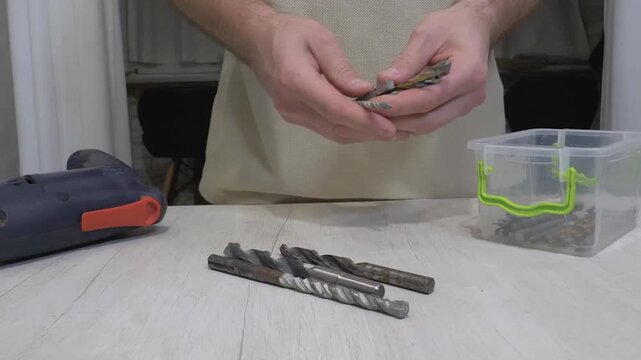  A worker lays out drills on a workbench. An electric drill and metal drill bits for drilling.