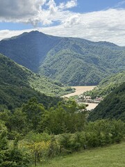 Fototapeta premium A scenic view of a river winding through lush green mountains under a partly cloudy sky. The landscape showcases natural beauty and tranquility.