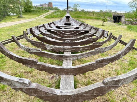 A front view showing the structural wooden ribs and skeleton framework of a historic Viking ship replica on display in a park in Latvia.