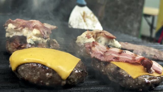 Burger patties topped with melted cheese, crispy bacon, and creamy blue cheese sauce while cooking on a hot grill. Gourmet street food preparation concept with premium ingredients and barbecue flavor