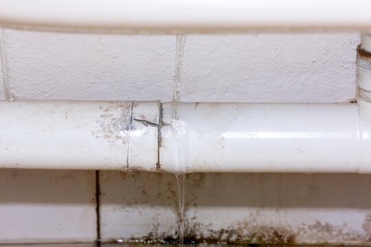 Water leak from a cracked white pipe in a bathroom, indicating plumbing issue and damage during repair work