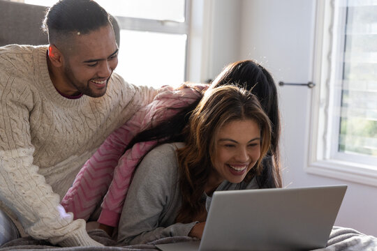 Family of three lying on bed, dad in cream sweater, child in pink hoodie watching laptop