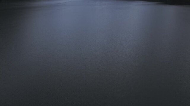 Calm aerial footage over the dark water surface of Multinskie Lakes, Altai Republic, Russia, surrounded by forested mountain slopes on an overcast day