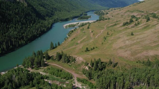 Drone footage of a winding river with sandbars between green mountains and open steppe slopes in Ak-Kem Valley, Altai Republic, Russia on a sunny summer day