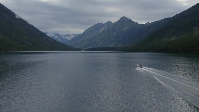 Wide scenic view of a speedboat leaving a wake on Multinskie Lakes, Altai Republic, Russia, surrounded by forested mountains and distant snowy peaks