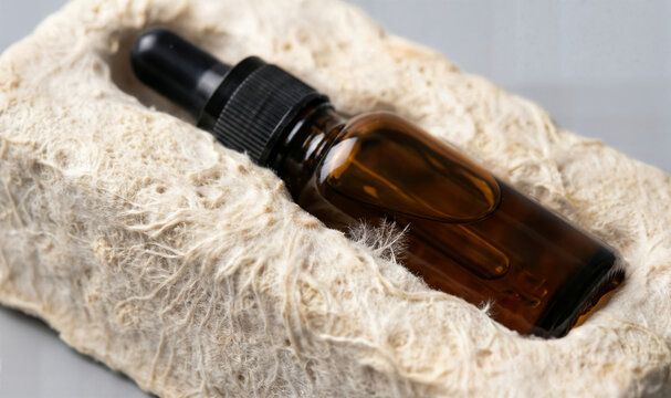 Amber glass dropper bottle filled with golden liquid rests in organic rough texture material on clean light background.