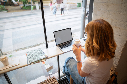Mature woman working remotely from coffee shop with laptop and takeaway coffee