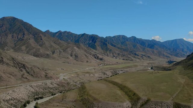Drone footage of Chuysky Trakt road winding through a wide mountain valley with rocky ridges and sparse steppe vegetation, Altai Republic, Russia