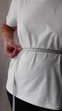 Senior woman measuring waist circumference with tape measure, weight management and healthy aging concept.