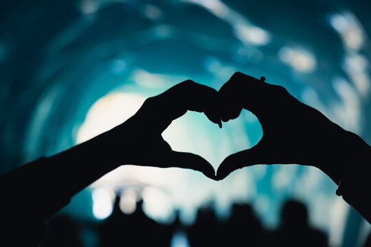 Heart hands silhouette in glowing blue glacier cave at Mer de Glace, France