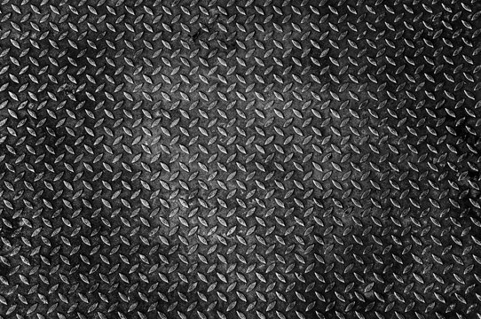 Close-up metallic diamond plate texture with weathered surface in dramatic dark lighting for industrial backgrounds