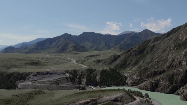 Wide landscape view of a winding highway and turquoise river in a rugged mountain valley on the Chuysky Trakt, Altai Republic, Russia, under clear blue sky