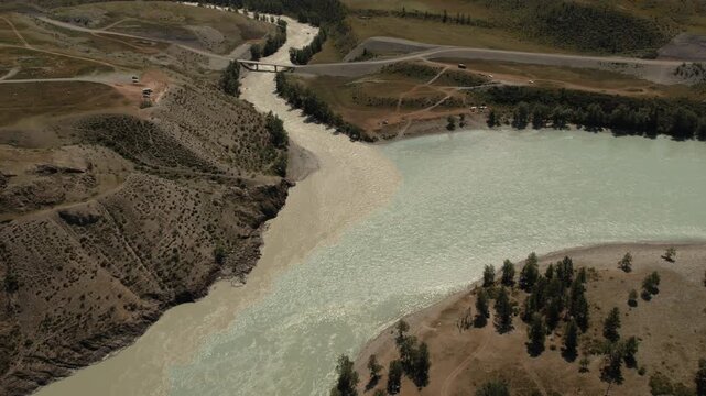 Drone footage of the Chuysky Trakt highway bridge crossing a wide mountain river, with steppe hills and forest patches in Altai Republic, Russia