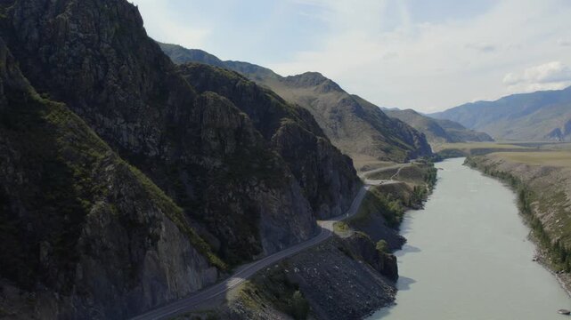 Drone footage of the Chuysky Trakt highway winding along the turquoise Katun River through rocky mountain canyon landscape in Altai Republic, Russia, sunny day