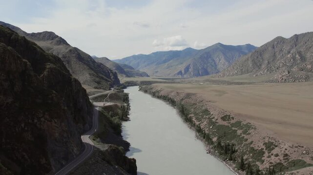 Drone footage of the Chuysky Trakt highway running beside the turquoise Katun River through a wide mountain valley in Altai Republic, Russia, on a bright summer day