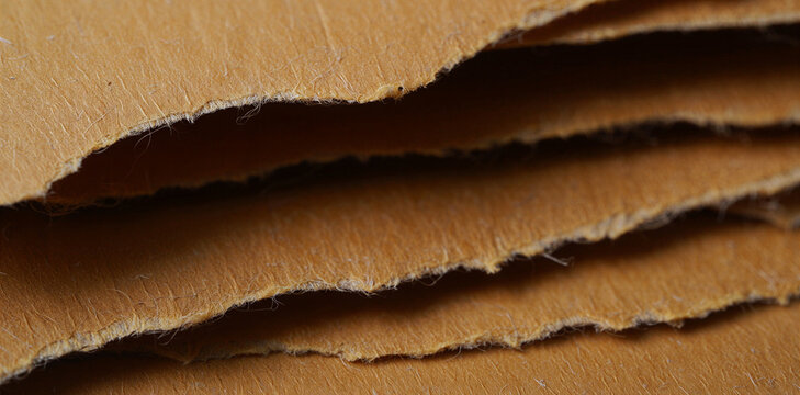 Stacked layers of torn brown craft paper showing fibrous edges with cardboard material background structure brownish recycled paperwork abstract paperboard creative stationery