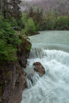 Water flows over rocks at Lechfall, Bad Faulenbach in Fuessen, Bayern, Germany. Nature surrounds the river and waterfall.